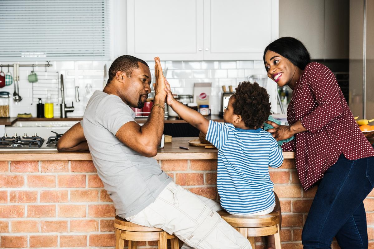 a kid high-fives a parent while another parent looks on after setting goals for successful family therapy