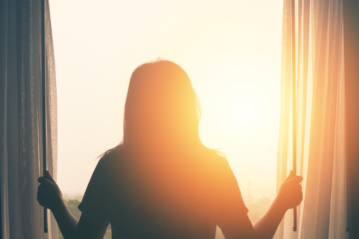 Coping Skills For Anxiety That You Should Know About woman looking out window into the dawn sun practicing coping skills for anxiety that you should know about