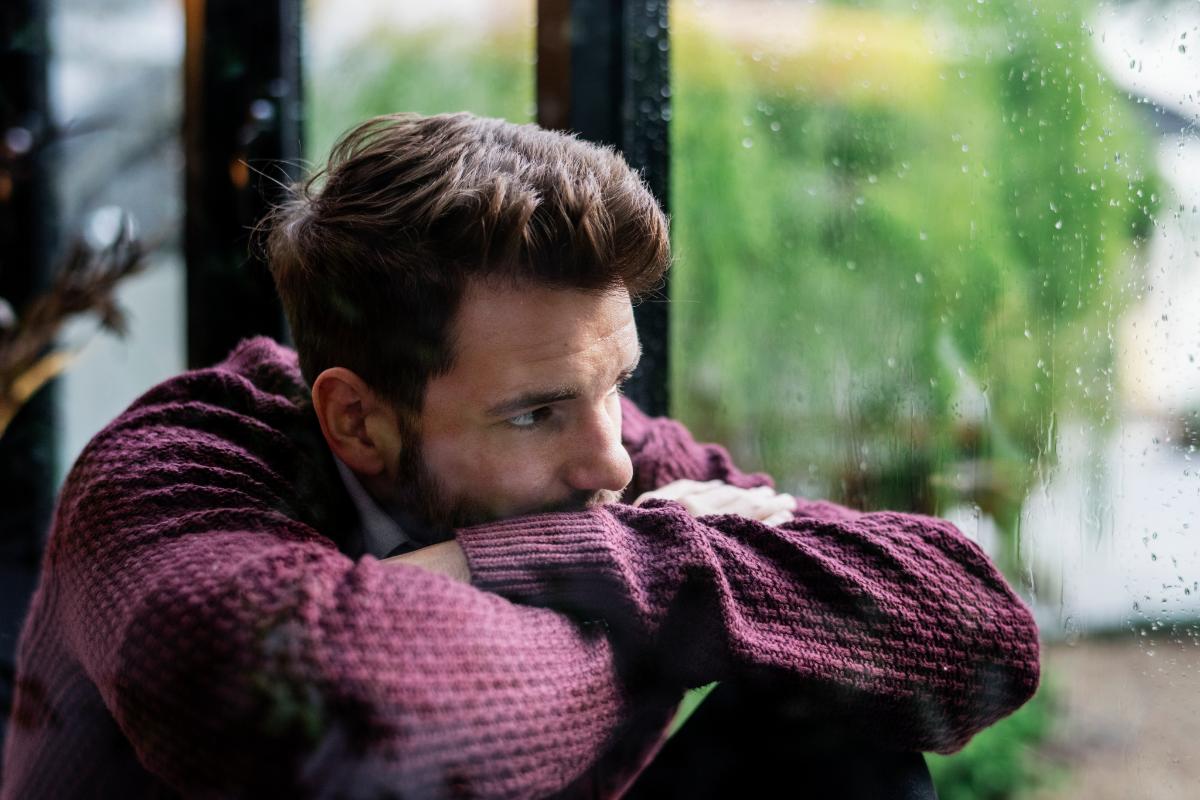 worried young man leaning on desk in front of window thinking about the effects of alcohol on mental health