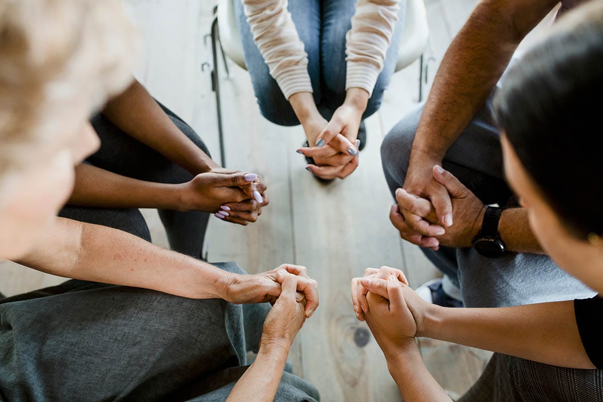 a group of people folds their hands in a circle in an intensive outpatient program treatment