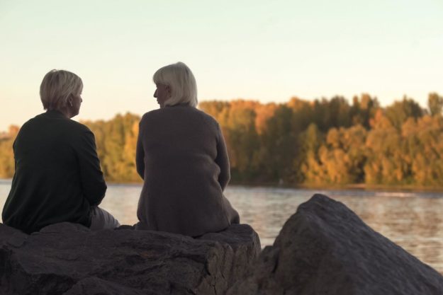 5 Anxiety Activities for Adults two elderly folks sit on a rock in front of a lake and talk about anxiety activities for adults