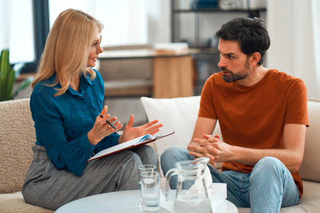 Benefits-of-Addiction-Therapy A man sits across from a counselor and understands the benefits of addiction therapy.